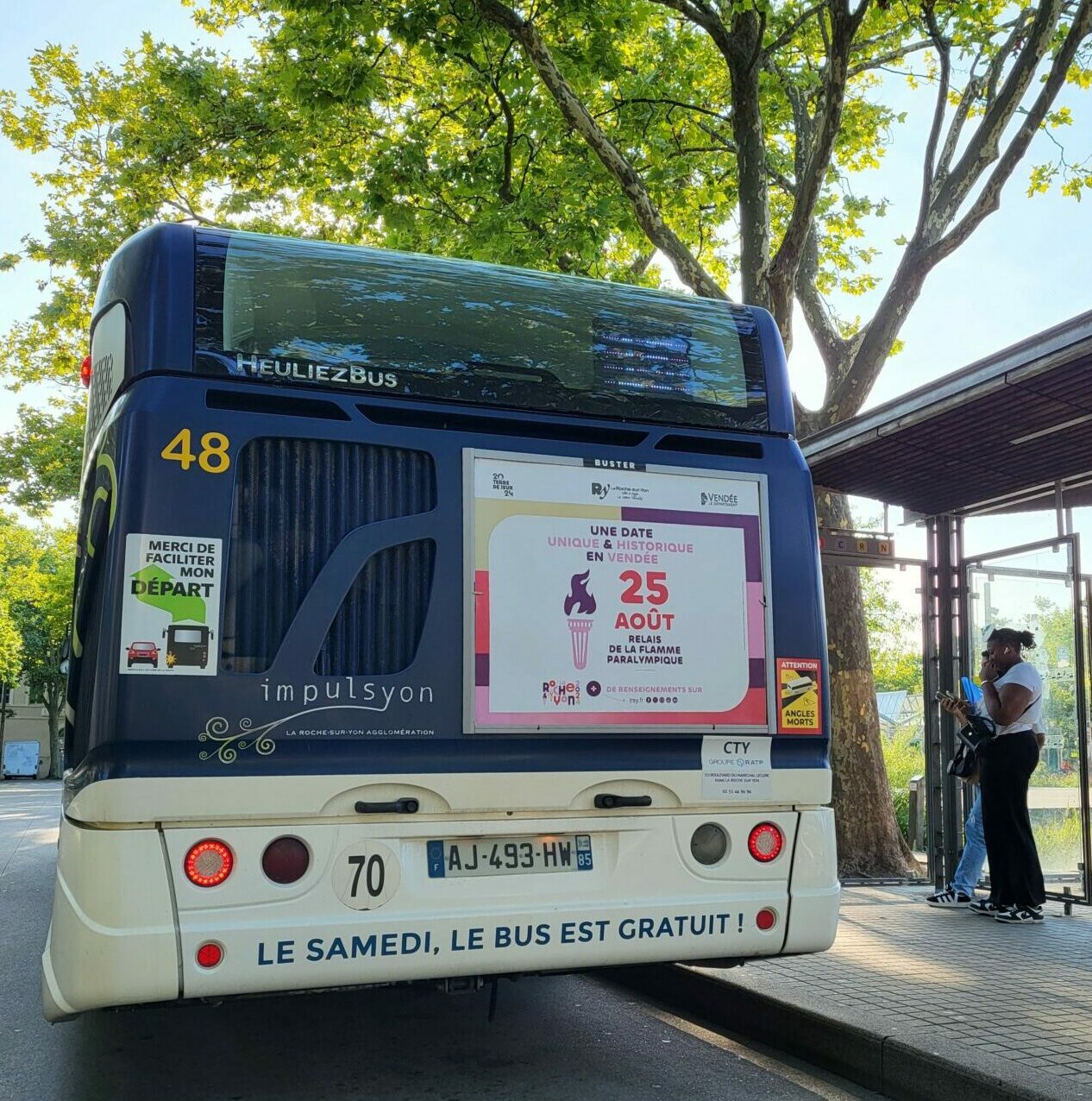Affichage publicitaire de la Flamme Olympique sur l’arrière d’un bus à La Roche-sur-Yon, captant l’attention des usagers de la route.